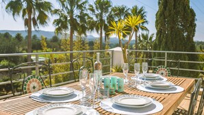 Una mesa lista para una comida, con platos, vasos y una botella, con vistas a un paisaje pintoresco de palmeras y montañas.