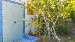 Un baño con zona de ducha revestida en azulejos azules, un pequeño banco y plantas en macetas distribuidas por el espacio.