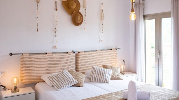 Una cama bien hecha con ropa de cama a rayas, una lámpara de noche y una ventana con cortinas.
