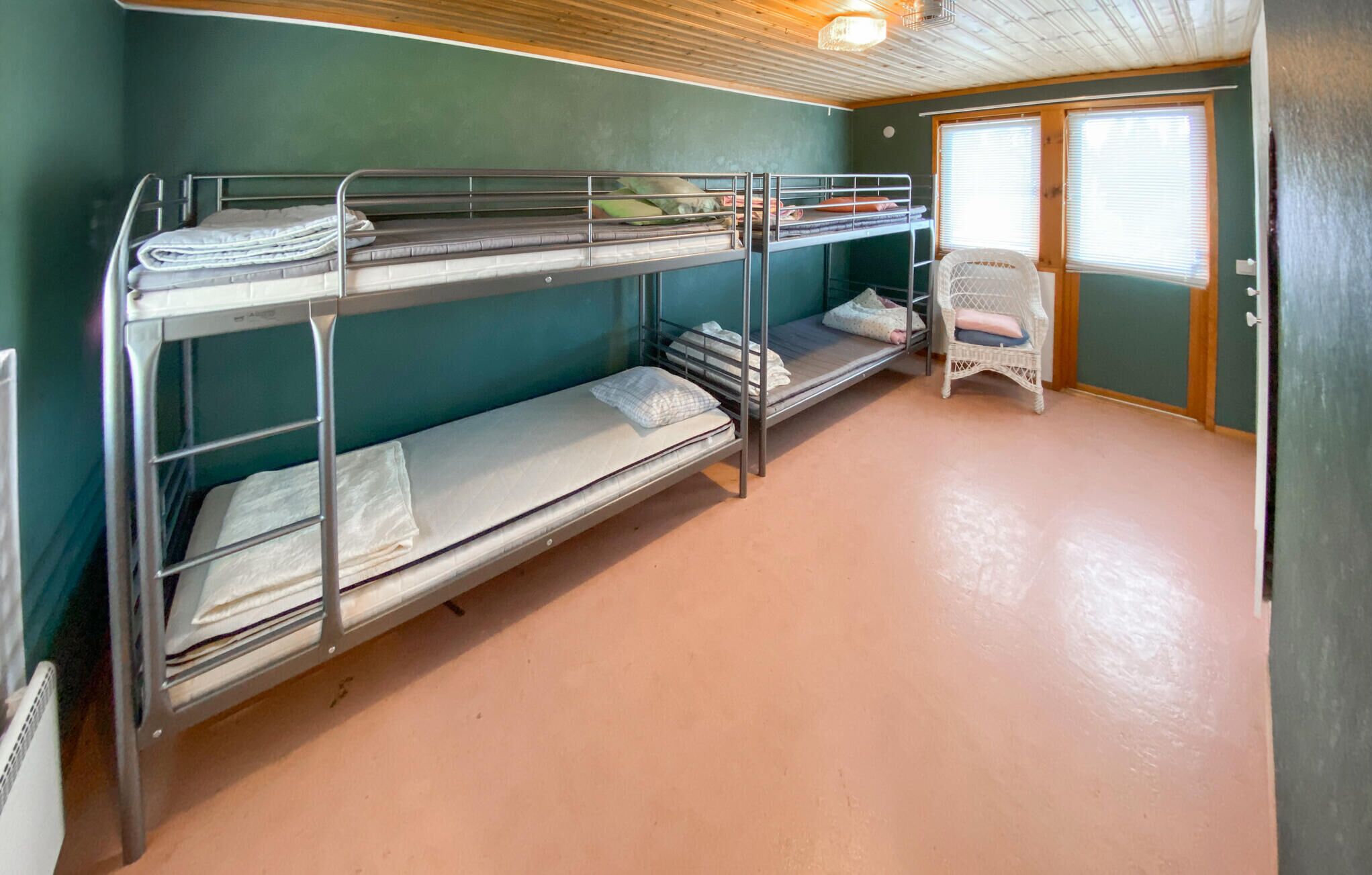 A bunk room with three bunk beds, a small white chair, and a window with blinds.