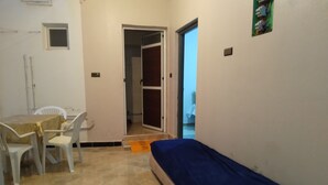 Una habitación pequeña con una cama individual, una mesa con sillas y una puerta que da a otra habitación.