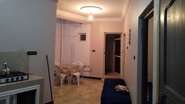 Un pasillo estrecho con un comedor que incluye una mesa, sillas, un sofá azul y una puerta que da a otra habitación.
