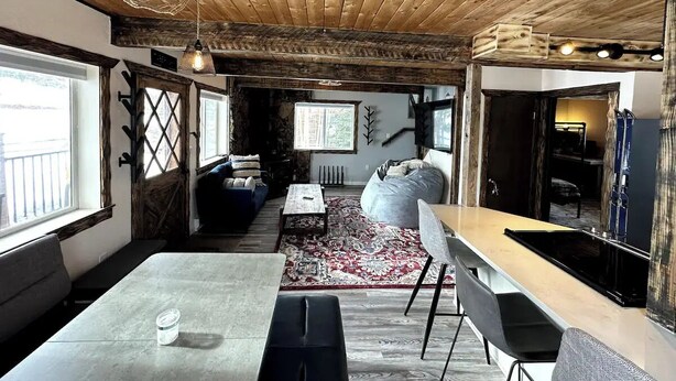 A rustic interior with a wooden ceiling, a dining table, a sofa, and a kitchen area. - Charming 3-bedroom Tabernash Tavern at Winter Park (Tabernash)