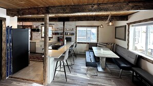 A rustic kitchen with wooden beams, a dining area with a bench, and a large window. - Charming 3-bedroom Tabernash Tavern at Winter Park (Tabernash)