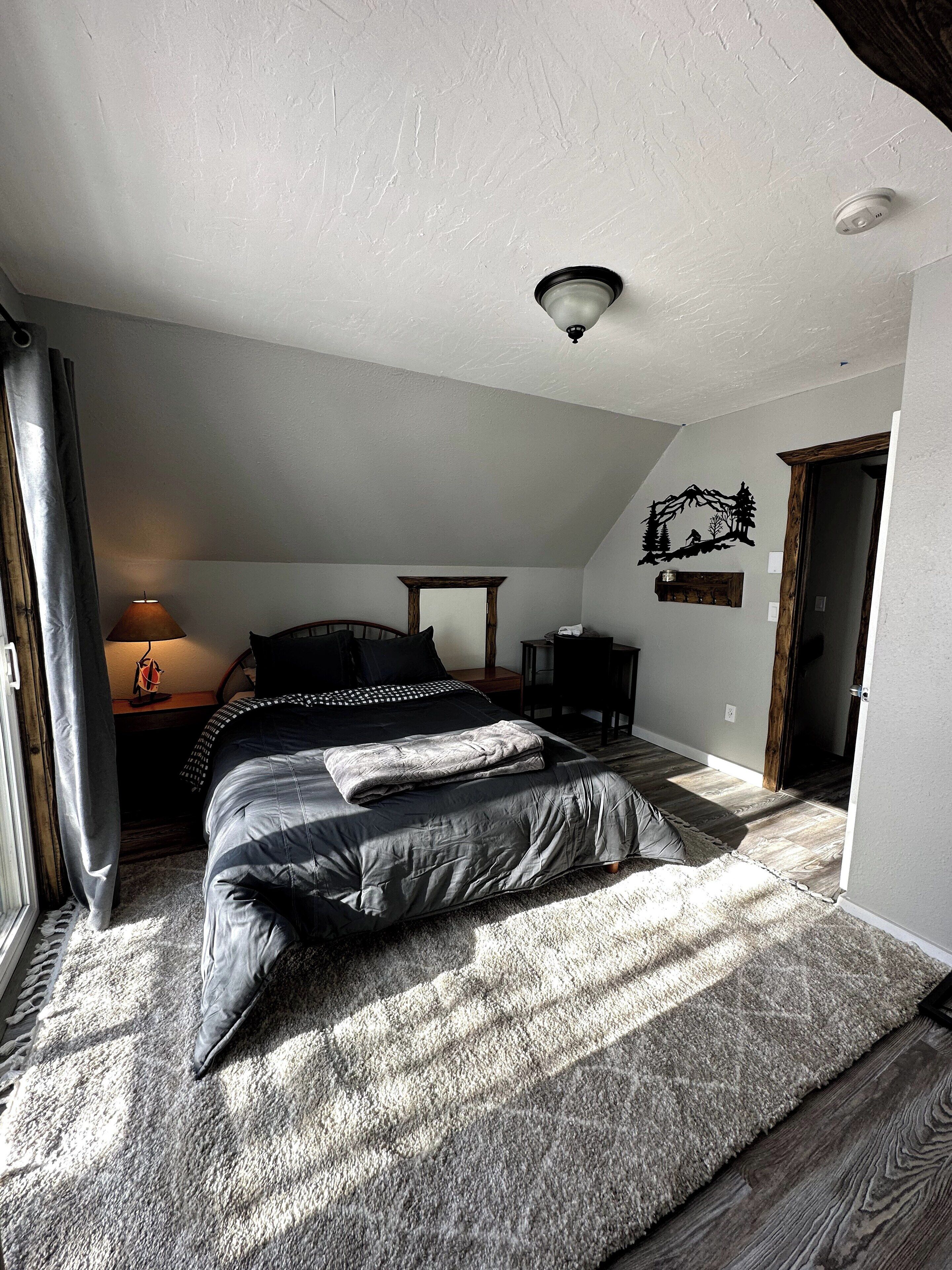 A bedroom with a bed, a nightstand, a lamp, a wall decoration, and a door.