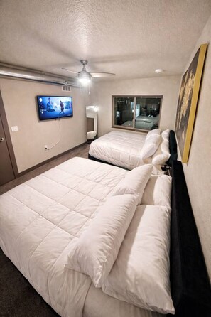 A hotel room with two beds, a ceiling fan, a TV, and a window.