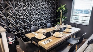 Un comedor con una pared de estampado geométrico, una mesa de madera dispuesta con platos, vasos y cubiertos, y sillas negras.