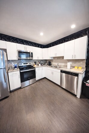 A modern kitchen with white cabinets, stainless steel appliances, and a wooden floor.