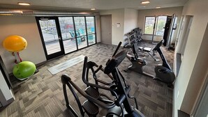 Un gimnasio con equipo de ejercicio, un ventanal y vista al estacionamiento.