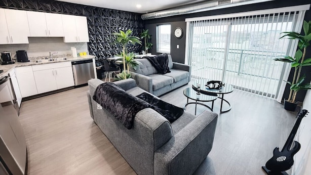 Un apartamento moderno con cocina, sofá gris, zona de comedor y balcón con vistas.