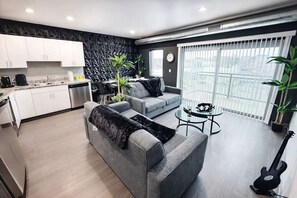 Eine moderne Wohnung mit Küche, grauem Sofa, Essbereich und einem Balkon mit Blick.