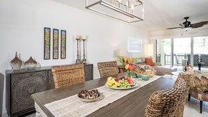A dining area with a wooden table, wicker chairs, and a decorative ceiling light. - Beachfront, Ocean Views, 2 bed, Poolside, Gym (St. Thomas)