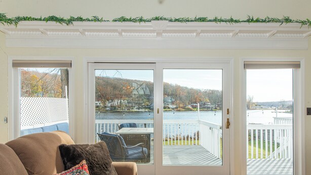 A living room with a sofa, a patterned pillow, and a view of a lake and dock through a sliding glass door. - Lake Front Home w/Dock, Kayak, Canoe Right On Lake Hopatcong w/AC Wifi Huge Deck (Jefferson Township)
