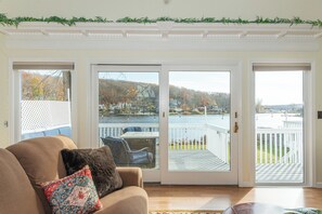 A living room with a sofa, a patterned pillow, and a view of a lake and dock through a sliding glass door.