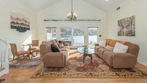 A spacious living room with a large window, a chandelier, and a patterned rug. - Lake Front Home w/Dock, Kayak, Canoe Right On Lake Hopatcong w/AC Wifi Huge Deck (Jefferson Township)