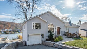 A two-story house with a white garage door, a front entrance with a small porch, and a landscaped front yard with a stone wall and a young tree. - Lake Front Home w/Dock, Kayak, Canoe Right On Lake Hopatcong w/AC Wifi Huge Deck (Jefferson Township)