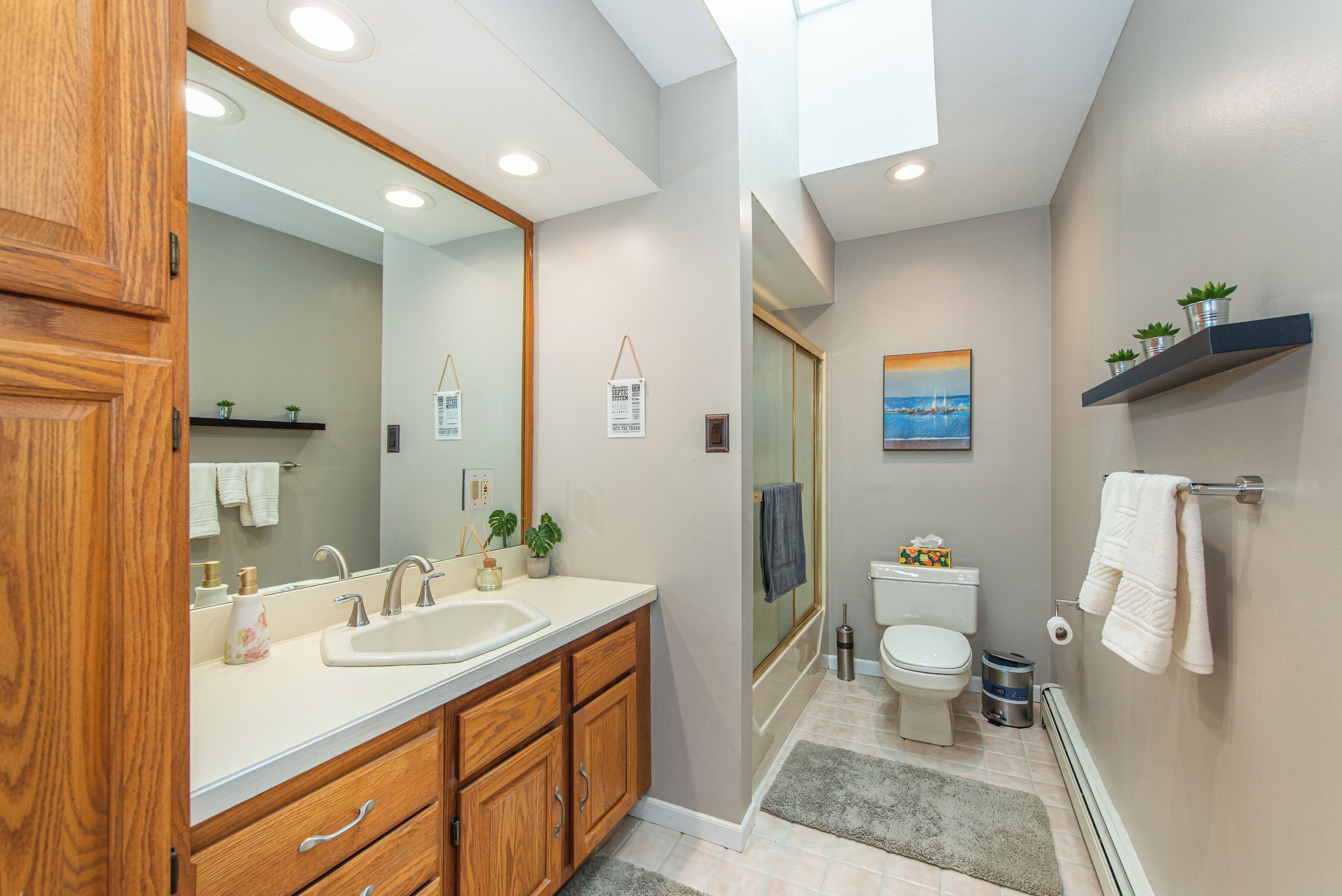 A modern bathroom with a wooden vanity, a large mirror, a shower, and a toilet.