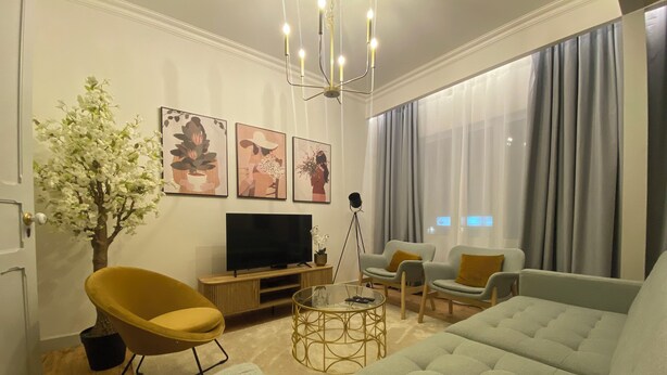 Una sala de estar moderna con un sofá grande de color gris, un sillón amarillo, un televisor de pantalla plana, una planta en maceta y obras de arte en la pared.