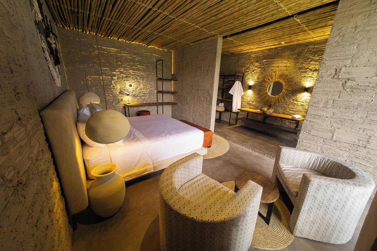 A modern bedroom with a large bed, bedside tables, and a small seating area with a bench and ottoman.