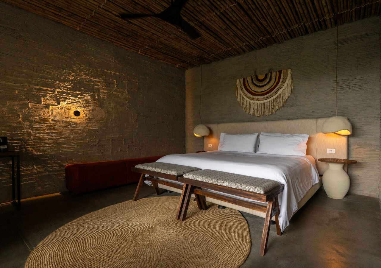 A bedroom with a bed, bench, wall-mounted lamp, and a woven rug.