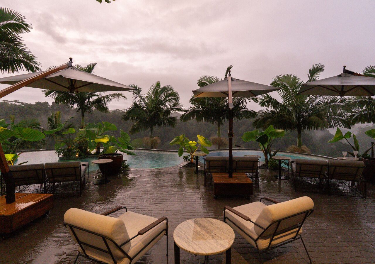 A wet outdoor area with tables and chairs, umbrellas, and a pool.