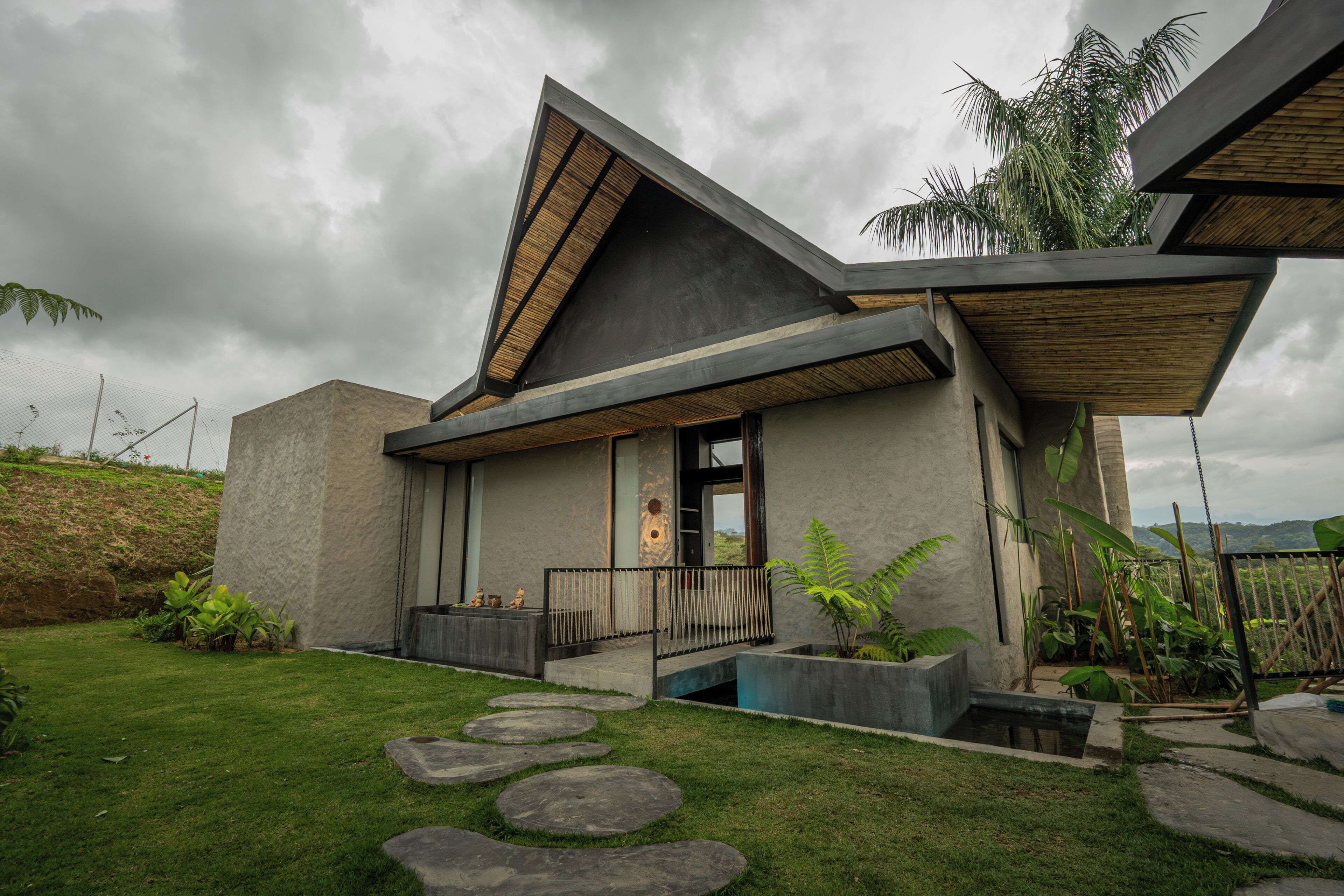 Una casa moderna con techo inclinado, fachada de concreto y un pequeño porche delantero.