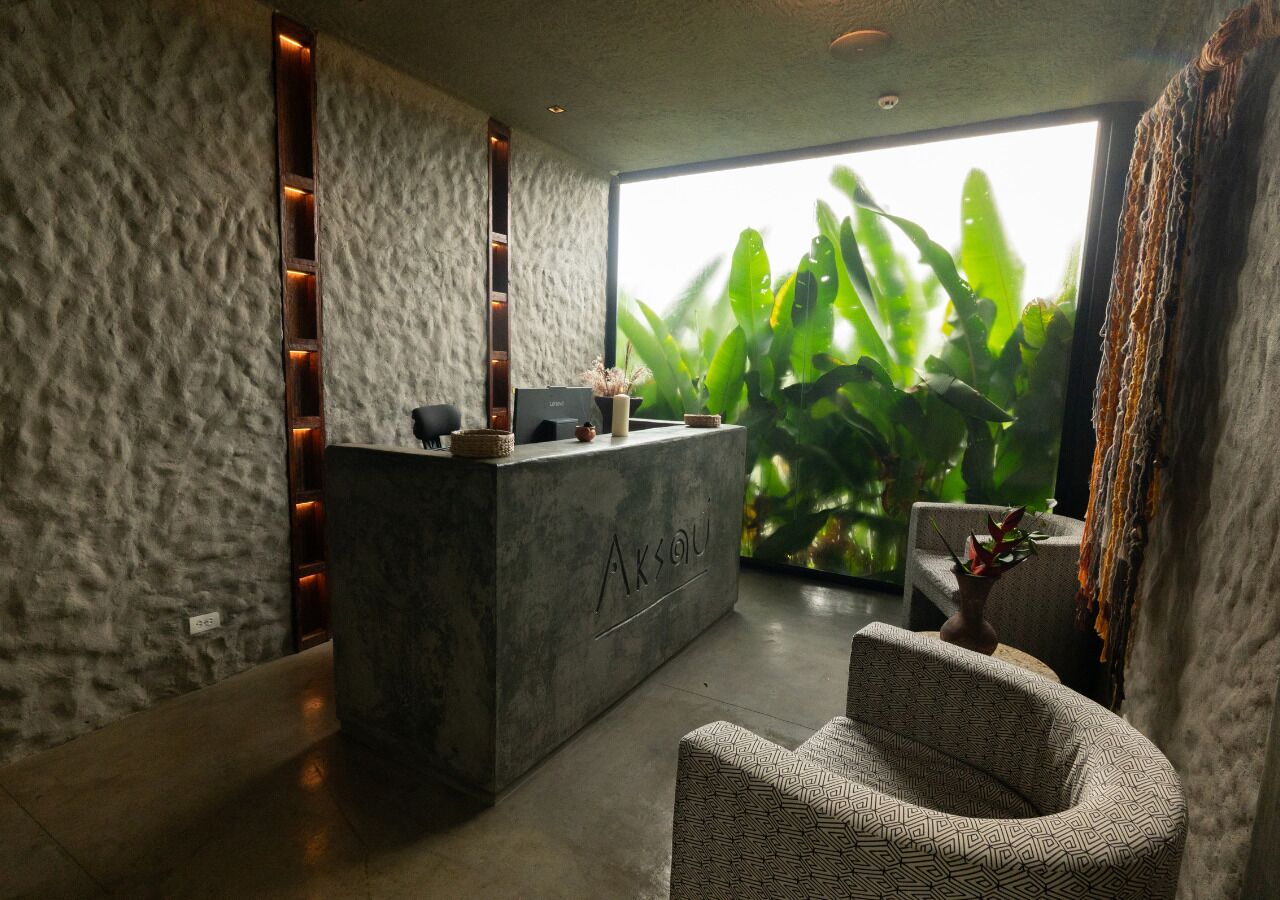 Una zona de recepción con mostrador de concreto, una silla estampada y un ventanal con vistas a zonas verdes.