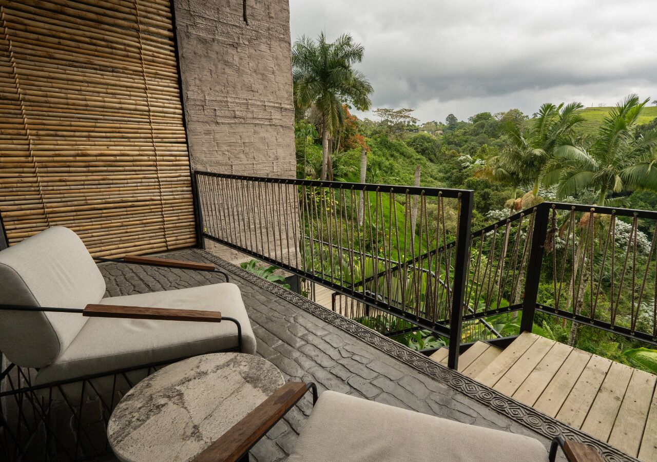 Un balcon avec deux fauteuils confortables, un mur en pierre et une vue sur une végétation luxuriante.