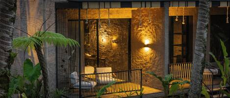 Un edificio moderno con fachada de piedra, un área de descanso con sillas y una mesa, y un interior bien iluminado.