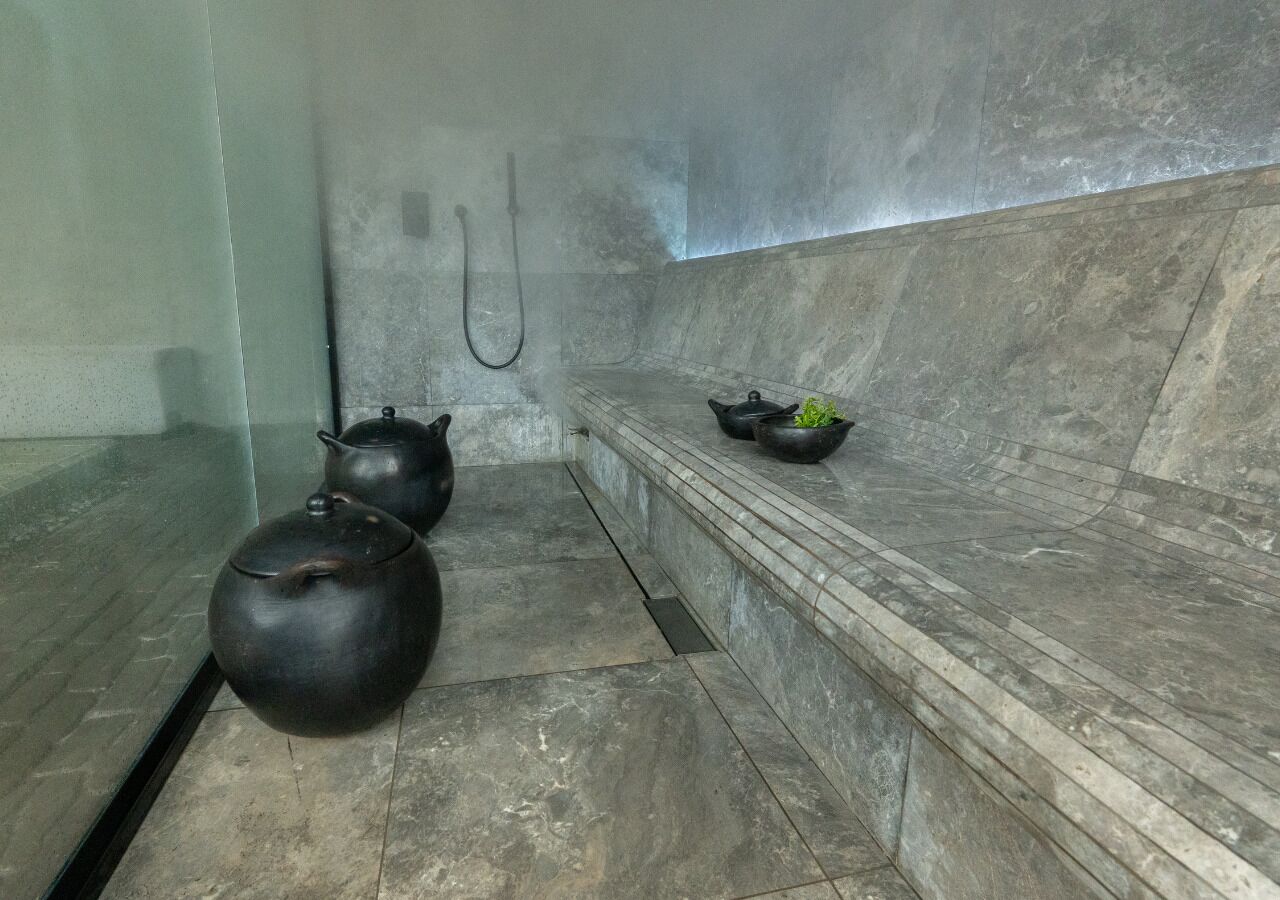 A bathroom with a tiled floor, a shower area, and a shelf with a teapot and a bowl.
