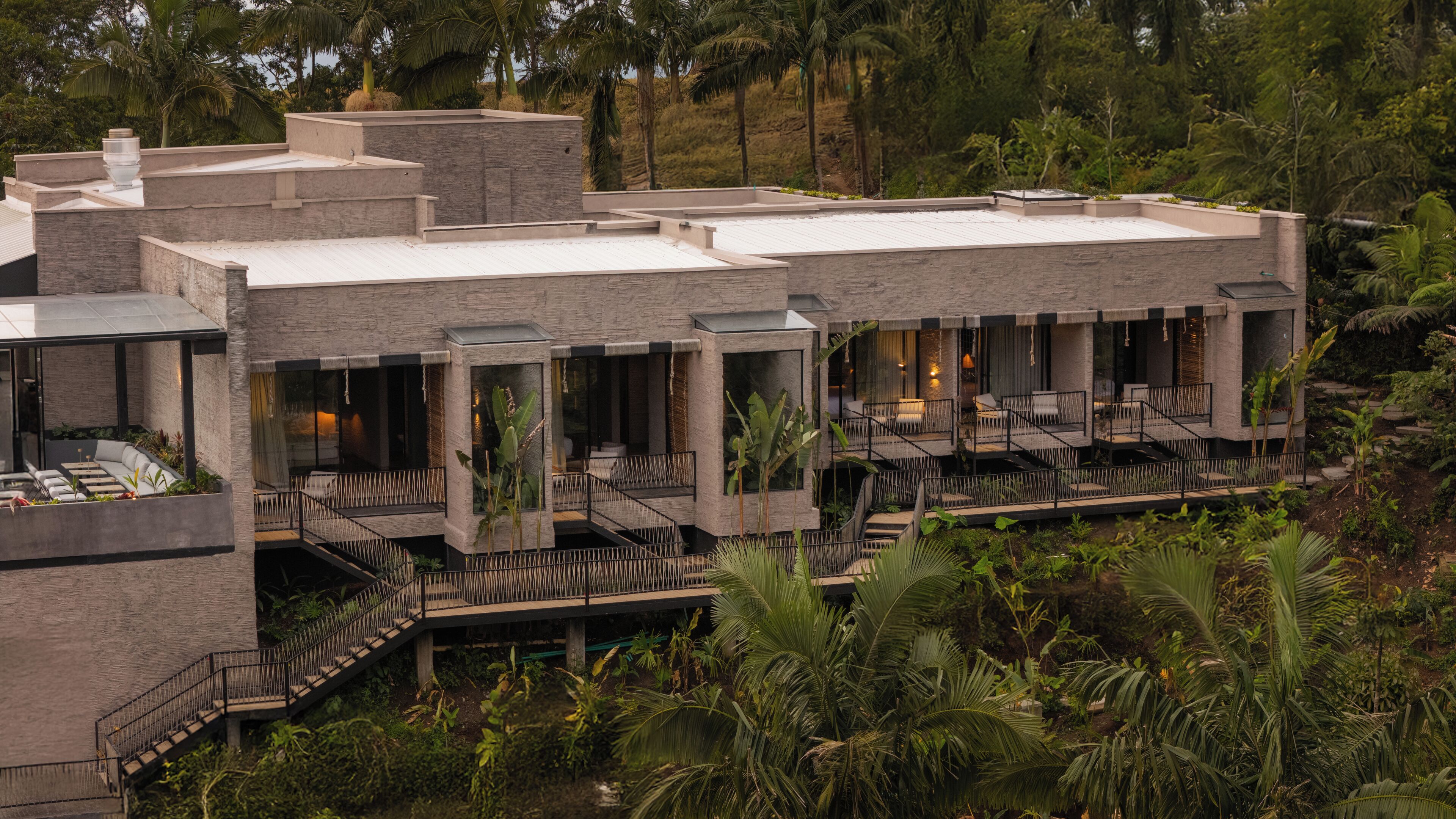 A modern hotel with multiple levels, outdoor seating areas, and lush greenery surrounding the property.