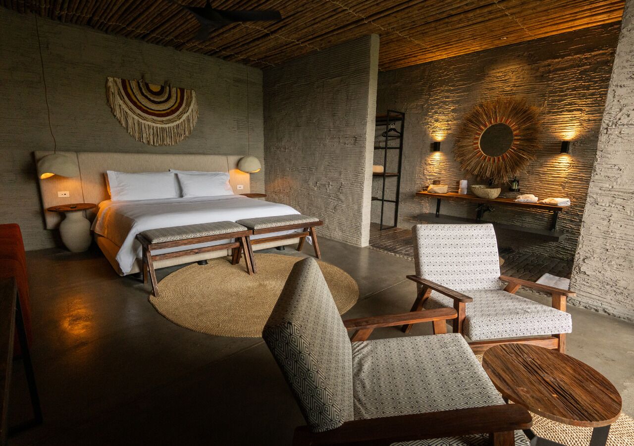 Une chambre à coucher moderne comprenant un lit, deux fauteuils, une petite table, une étagère fixée au mur et un miroir décoratif.
