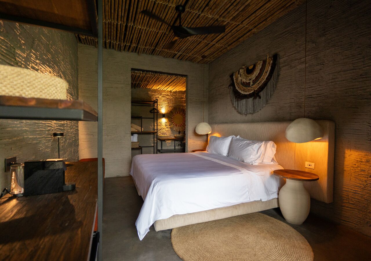 Quarto com cama, mesas de cabeceira, luminária e um objeto decorativo na parede.