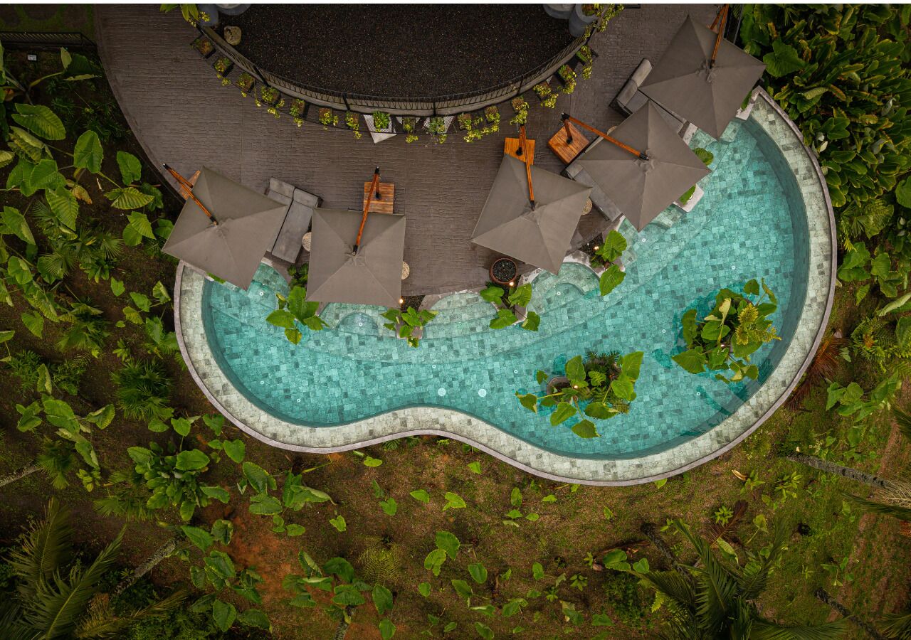 A circular pool with surrounding greenery, wooden seating, and umbrellas.
