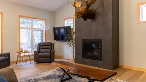 Un salon moderne avec une cheminée, une tête de cerf décorative accrochée au mur et un téléviseur.