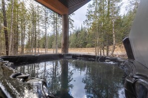 A hot tub area with a wooden deck and a forest view. - Ski In Mountain Retreat with Hot Tub (Fernie)