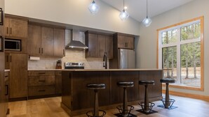 Une cuisine moderne avec des meubles en bois, un réfrigérateur en acier inoxydable, un four à micro-ondes et un grand îlot central doté de tabourets de bar.