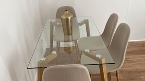 Une table à manger moderne, dotée d’un plateau en verre et de pieds en bois, entourée de quatre chaises rembourrées.
