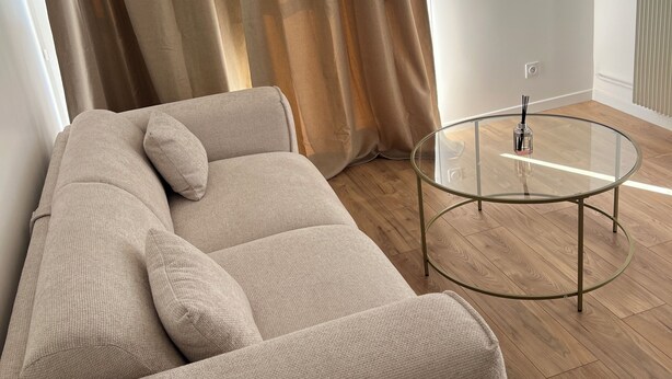 Un salon moderne avec un canapé beige, une table basse en verre et un plancher en bois.