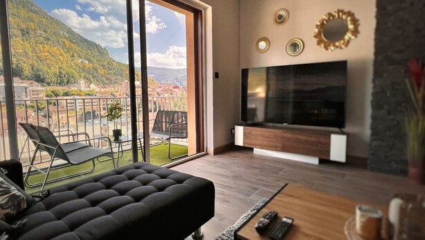 Un salon moderne doté d’un grand téléviseur, d’un canapé et d’un balcon offrant une vue sur une région montagneuse.