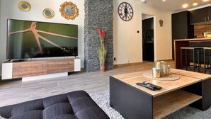 Un salon moderne doté d’un téléviseur à écran plat, d’un mur décoratif en pierre, de miroirs décoratifs et d’un coin repas avec une table et des chaises en bois.