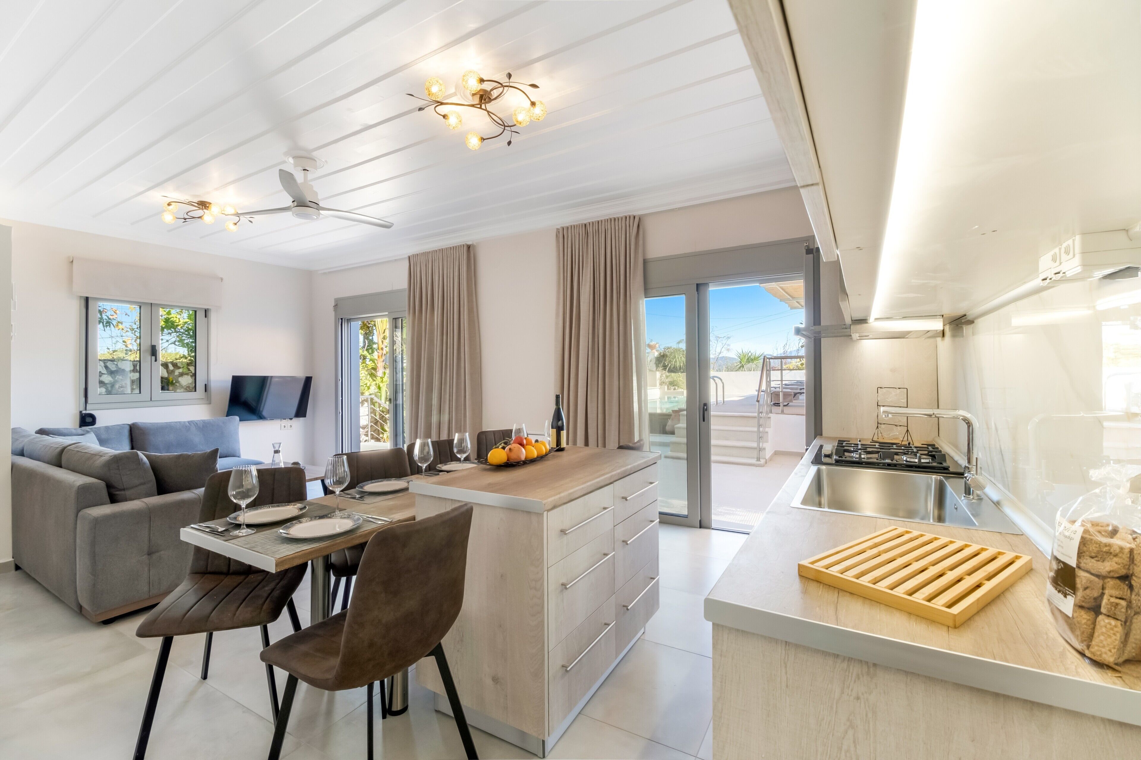 A modern kitchen with a central island, a dining area with a sofa, and a TV mounted on the wall.