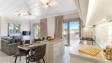 A modern kitchen with a central island, a dining area with a sofa, and a TV mounted on the wall.
