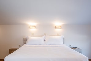 A neatly made bed with white linens, two bedside lamps, and a nightstand with a book.