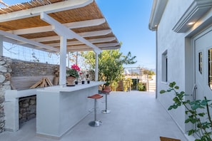 A covered outdoor area with a stone wall, a bar with stools, and potted plants.