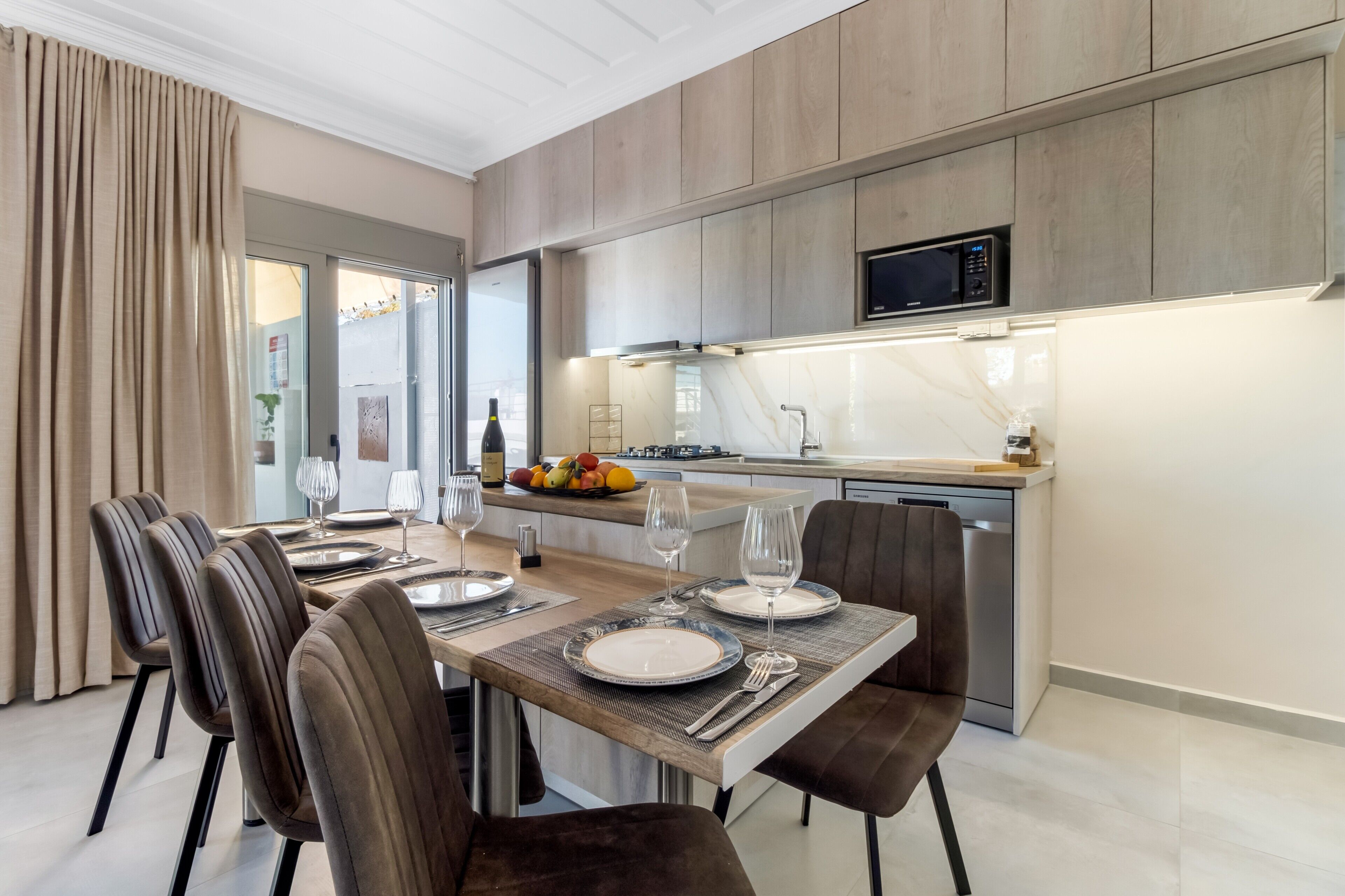 A modern kitchen with a dining area, wooden cabinets, a microwave, and a fruit bowl.