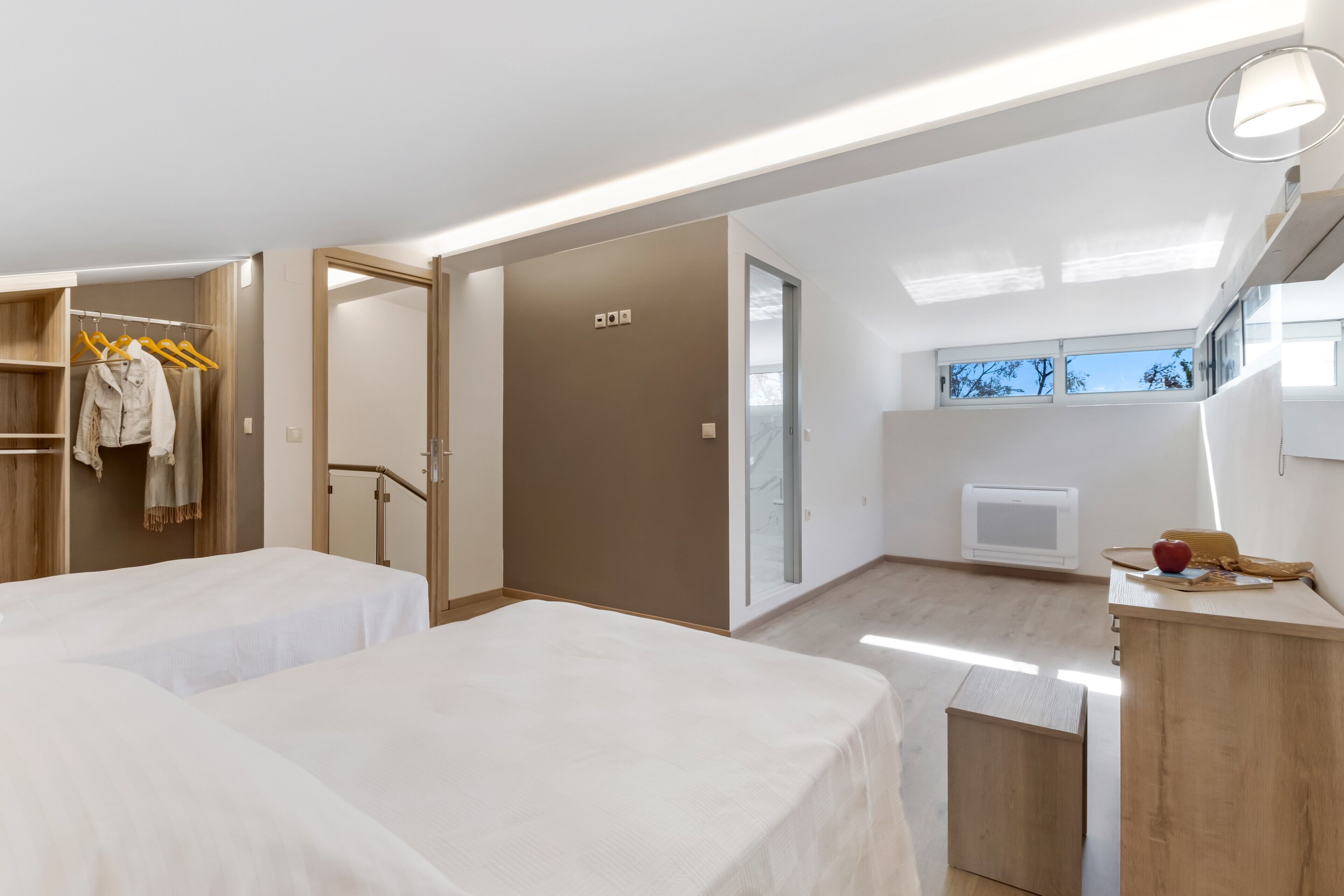 A modern hotel room with two beds, a walk-in closet, a small kitchenette, and a view of the outdoors.