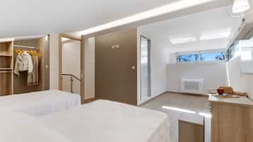 A modern hotel room with two beds, a walk-in closet, a small kitchenette, and a view of the outdoors.