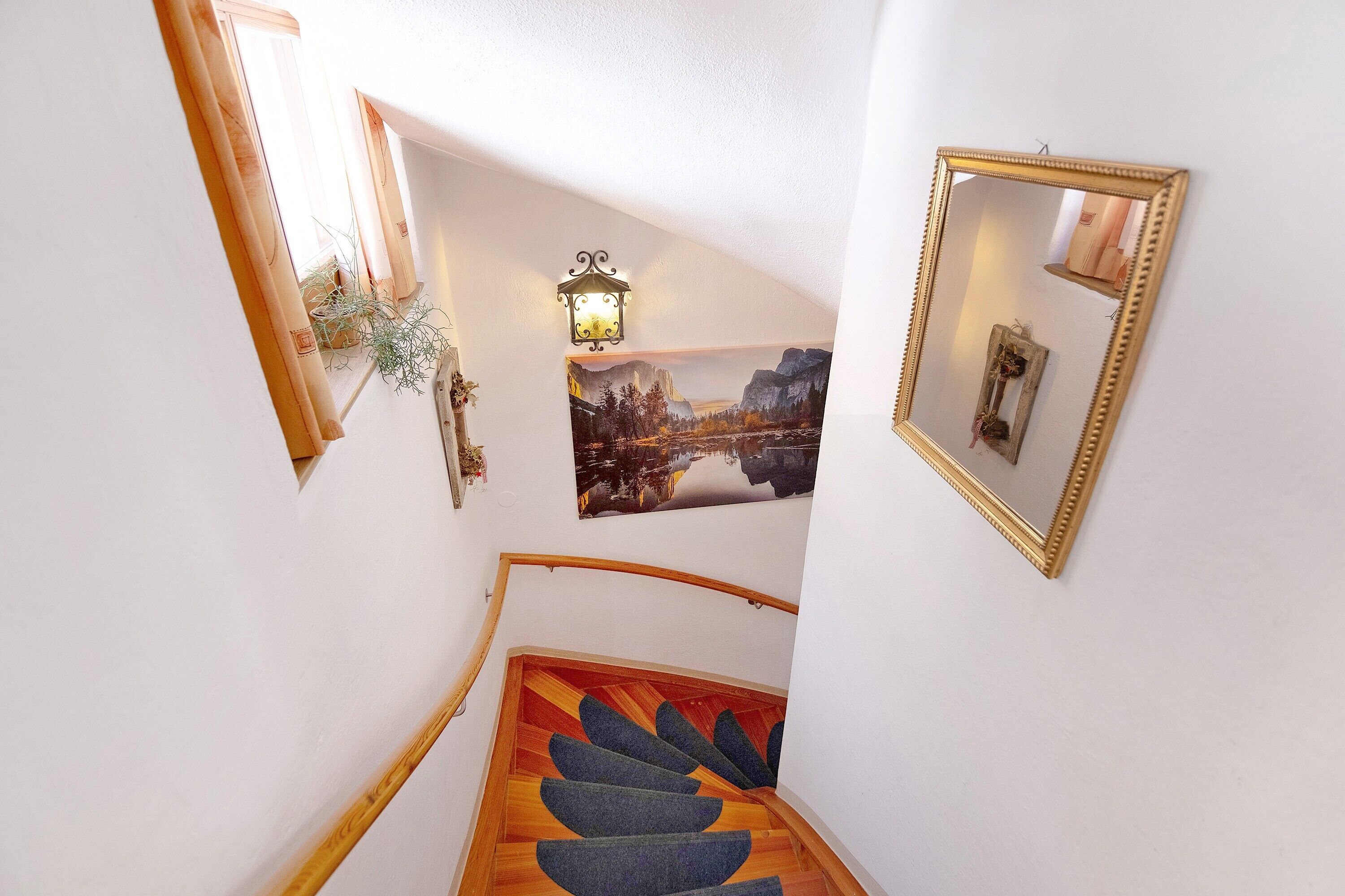 Una escalera con barandilla de madera y peldaños alfombrados, un aplique de pared y un cuadro de paisaje enmarcado.