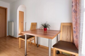 A dining area with a wooden table, two chairs, a potted plant, and a radiator.